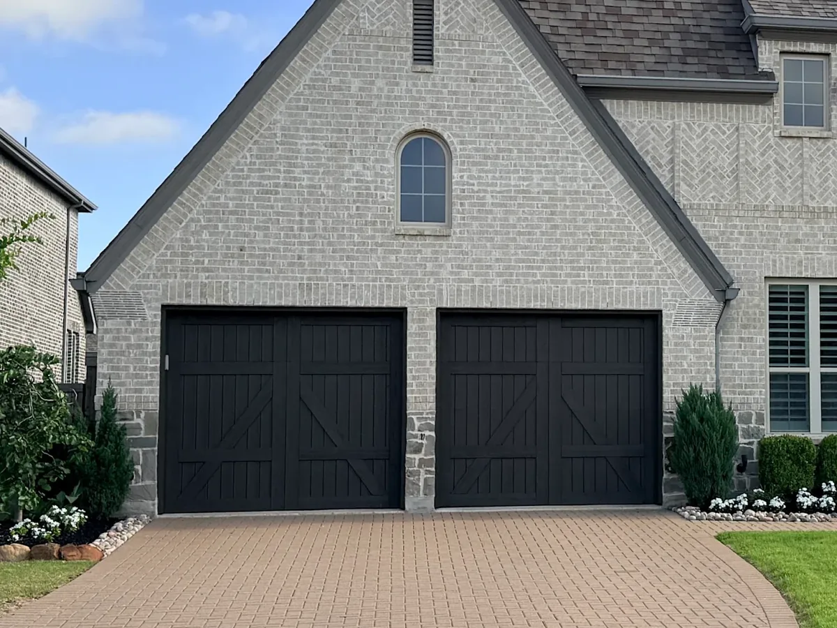 White brick home with two black carriage garage doors